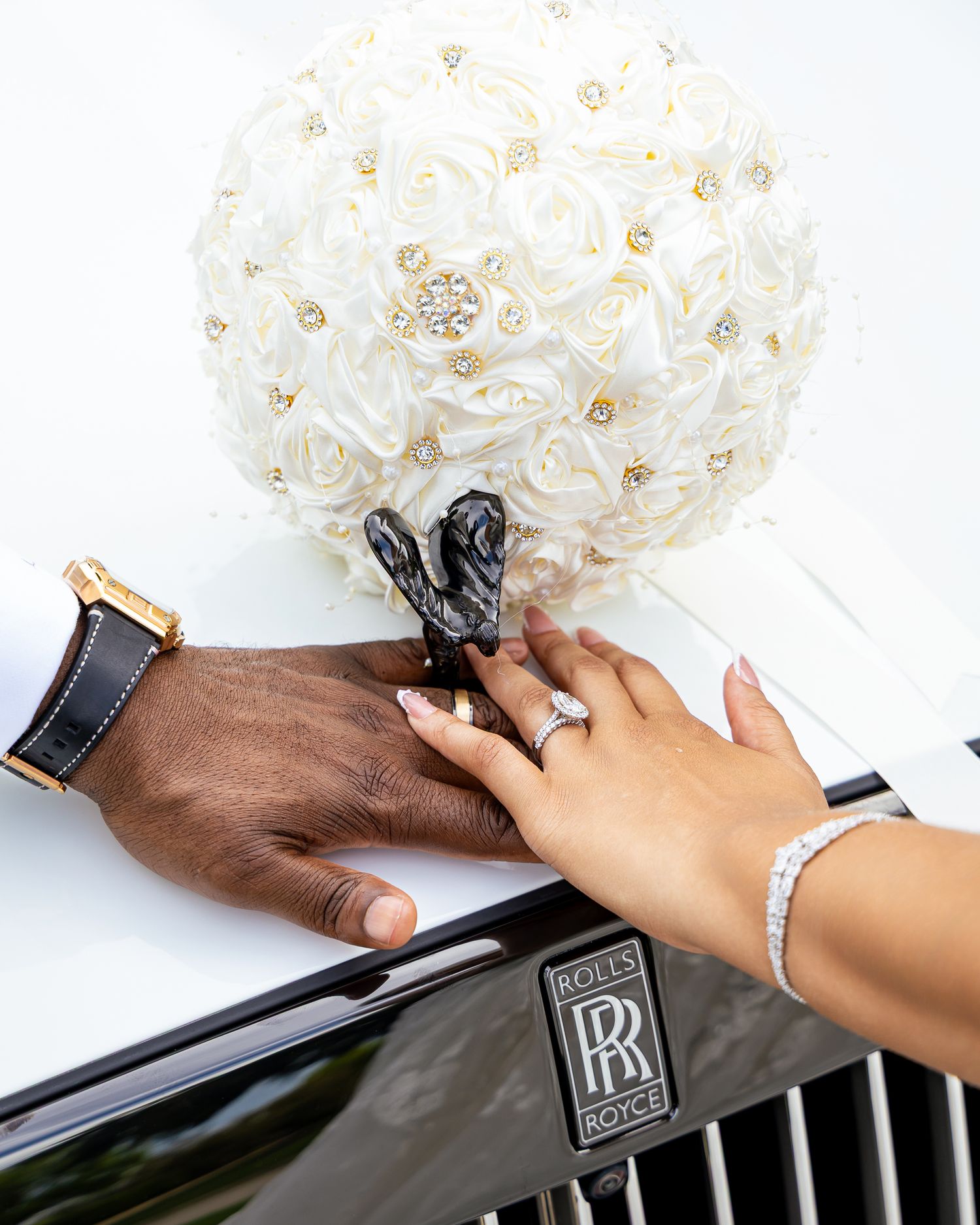 Two hands attach a silver hood ornament emblem onto a black luxury car surface.