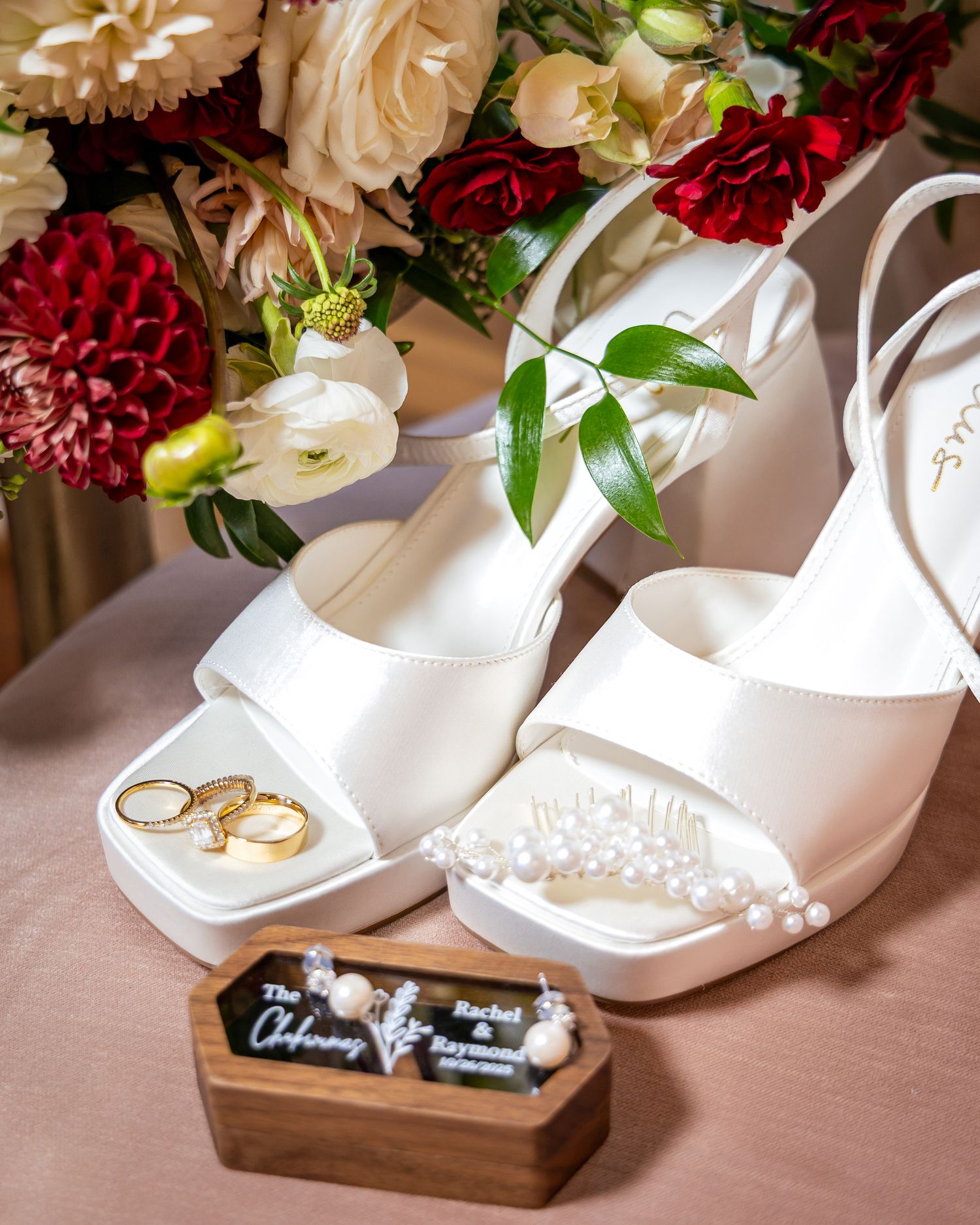White wedding shoes and rings displayed with floral arrangements and wooden ring boxes for wedding photography.