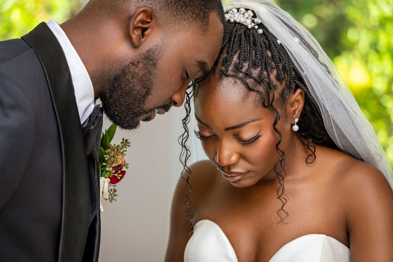 A romantic wedding couple shares an intimate moment together in a garden setting with natural sunlight.