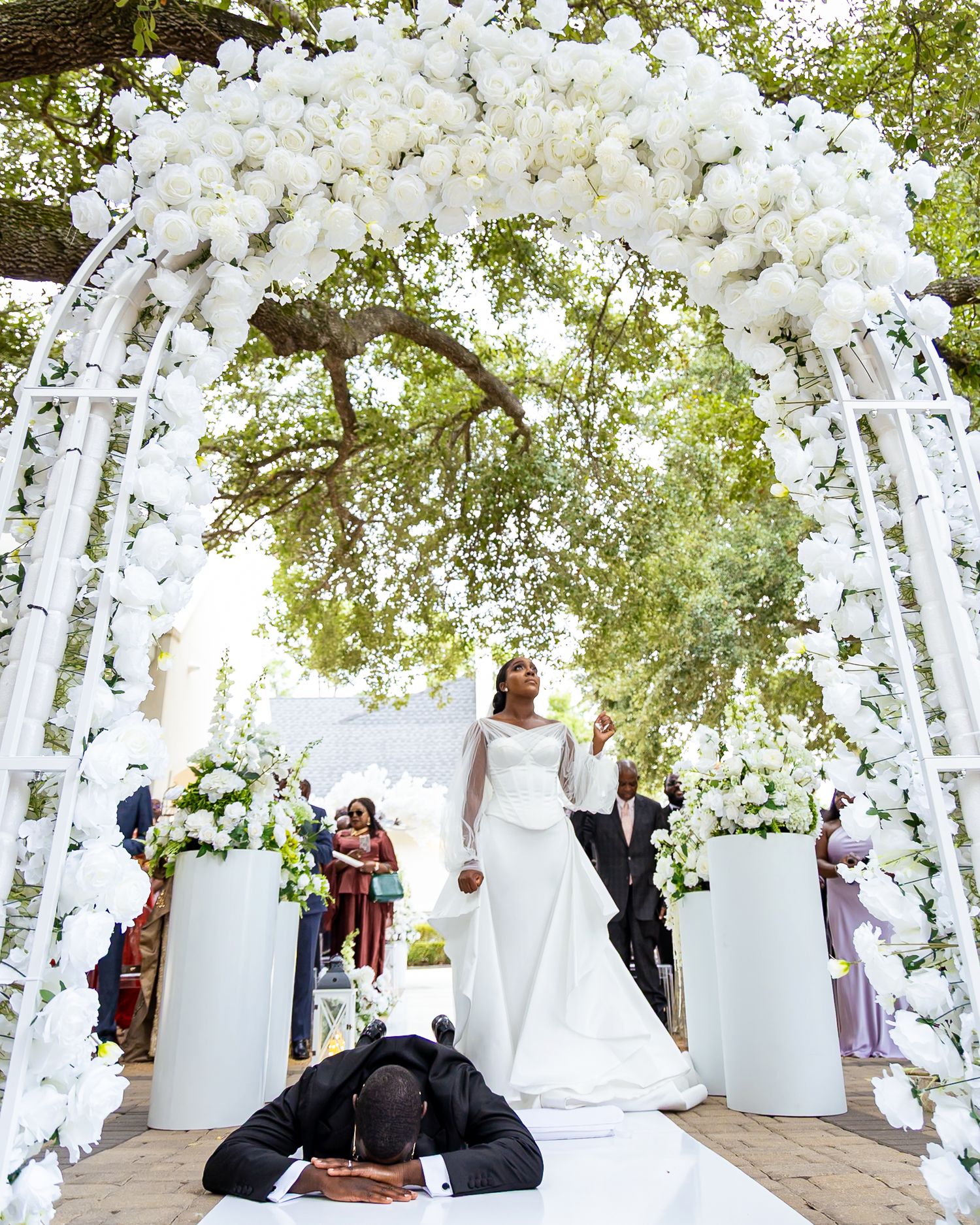 A wedding ceremony venue decorated with white floral arches and trees creating an enchanted garden atmosphere.