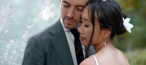 Romantic couple in wedding attire sharing an intimate moment outdoors, bride wearing white flower in hair.