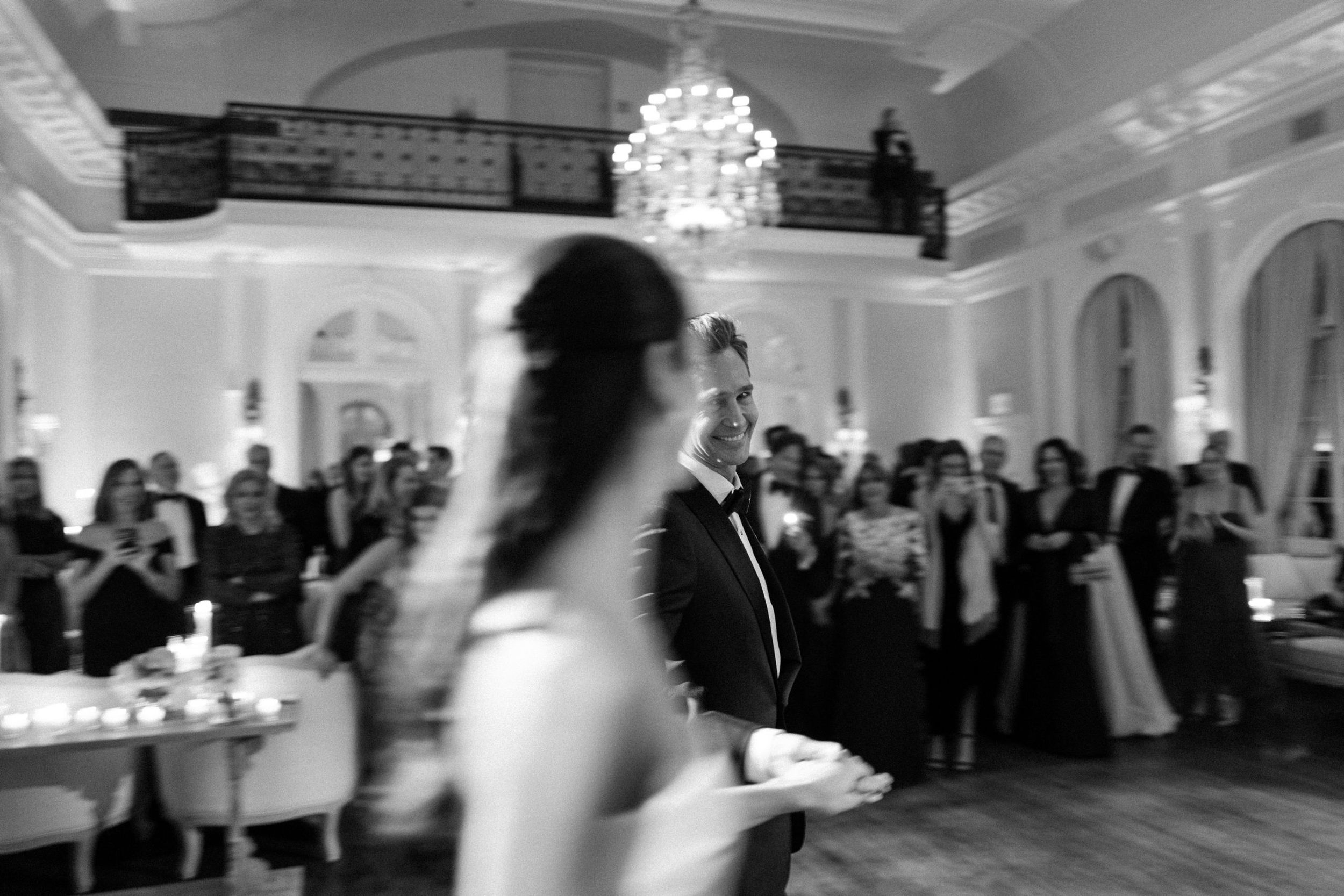 An elegant black and white wedding reception scene in a grand ballroom with crystal chandelier.