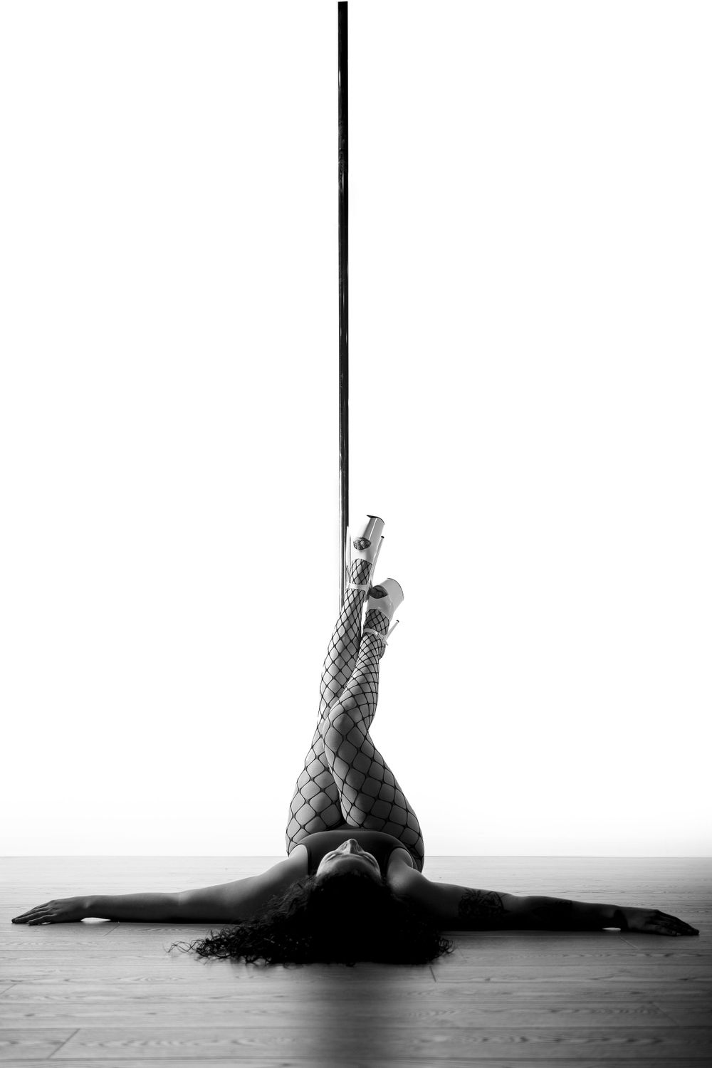 Artistic black and white photo of pole dance splits pose on wooden floor.