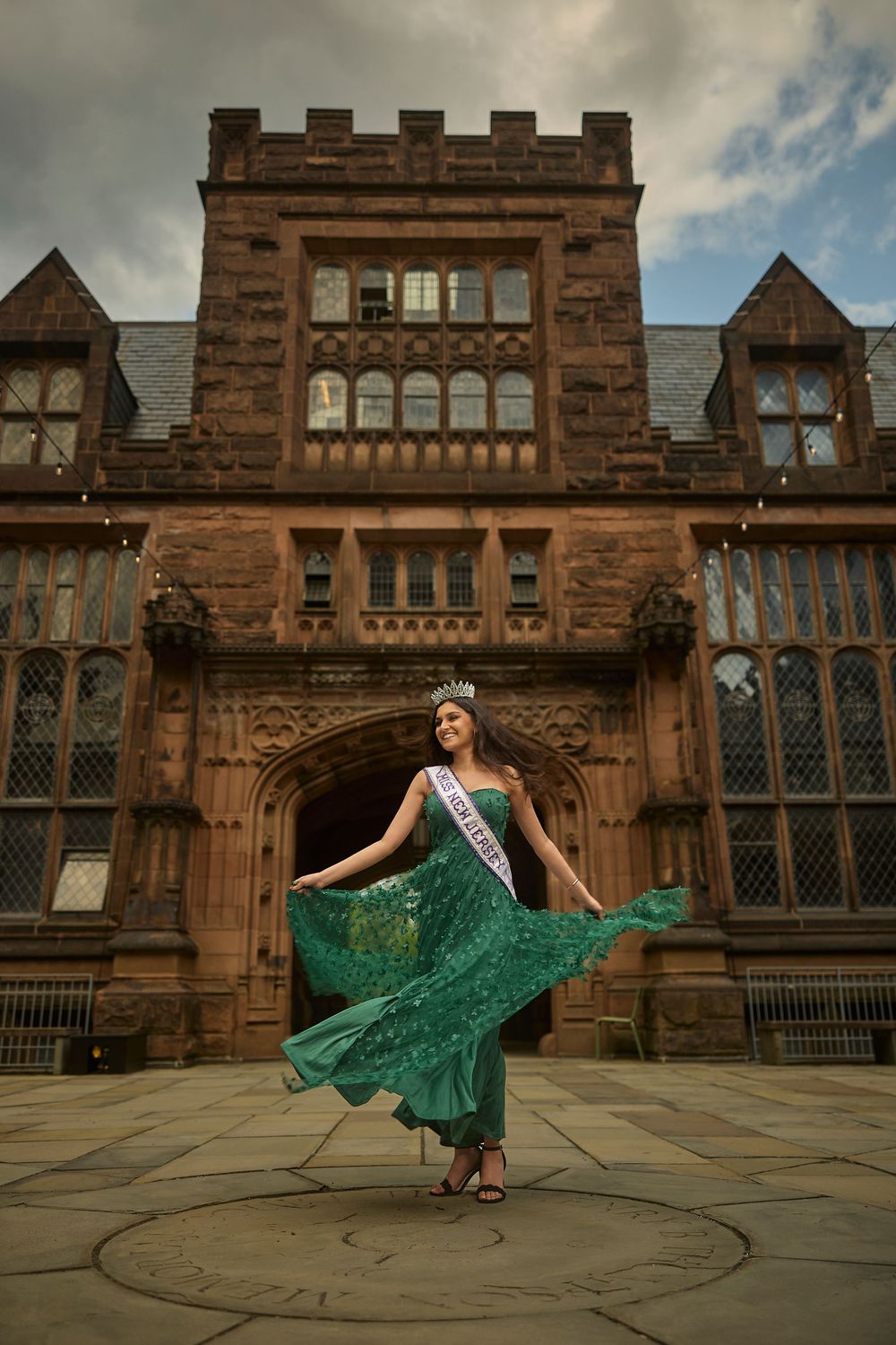 A flowing emerald green dress twirls gracefully against the backdrop of a historic Gothic stone building.