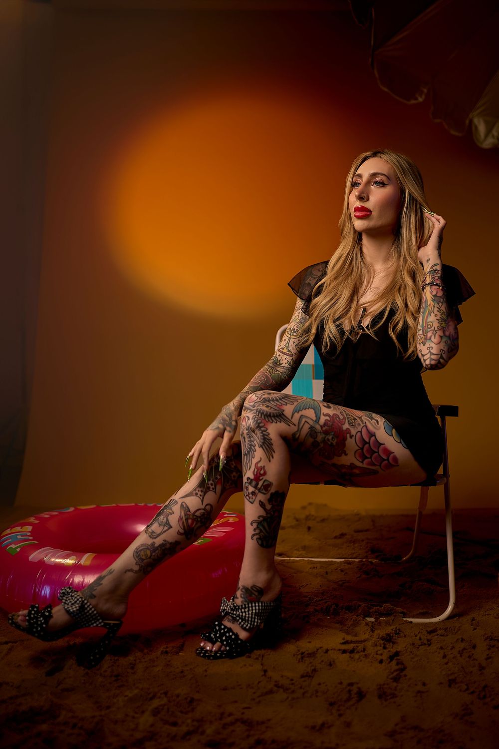 Fashion model in black lace poses on dark backdrop with dramatic orange lighting and vintage aesthetic.
