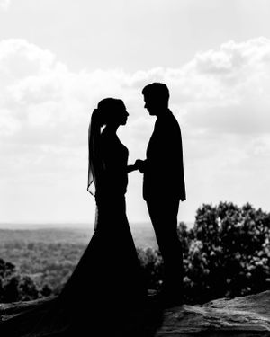 Black and white silhouette of couple in wedding attire standing on cliff edge. Middle TN wedding photographer.