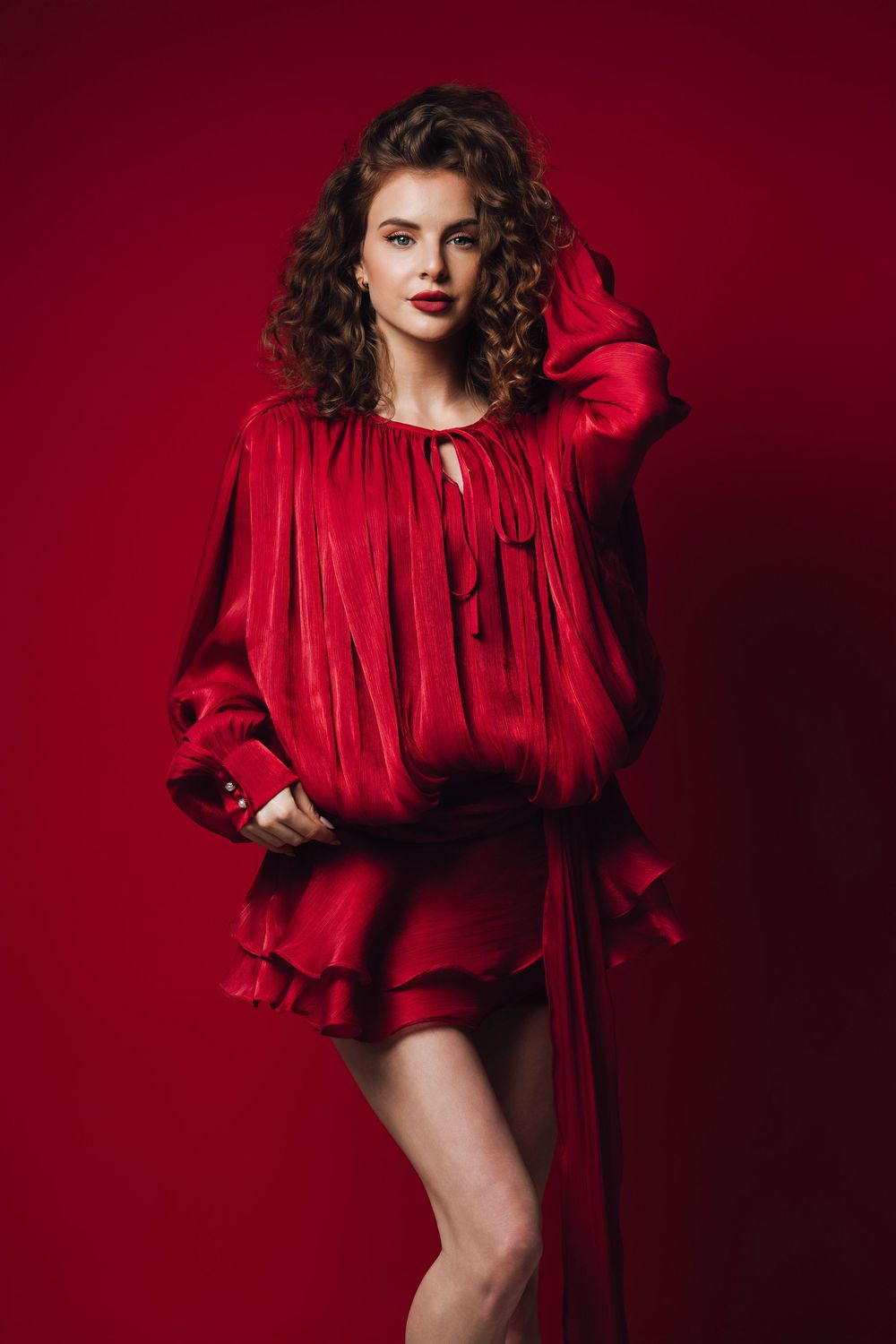 Dramatic fashion shoot featuring model in red ruffled dress against burgundy background.