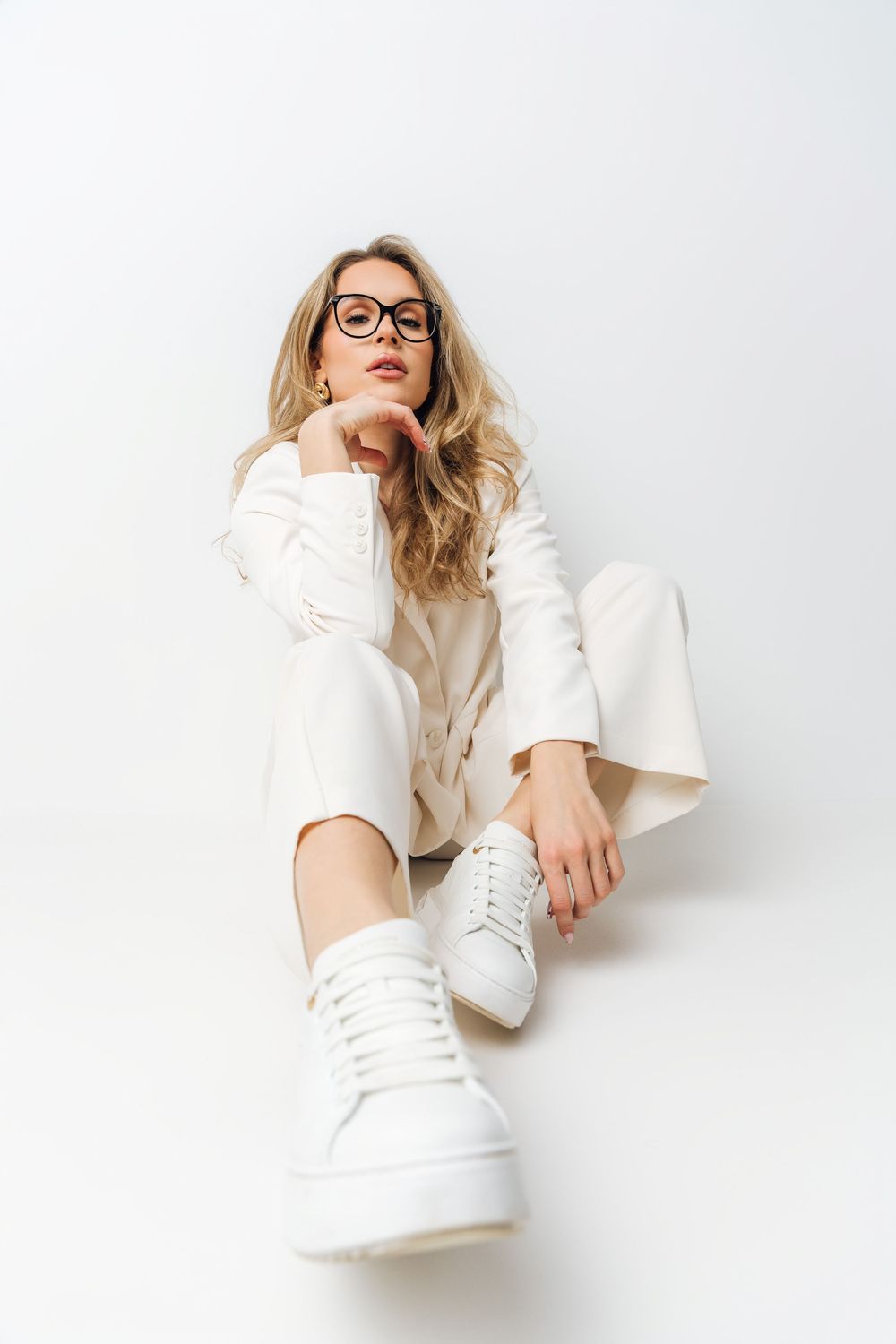 Stylish white monochromatic fashion shoot with model in glasses against light background.