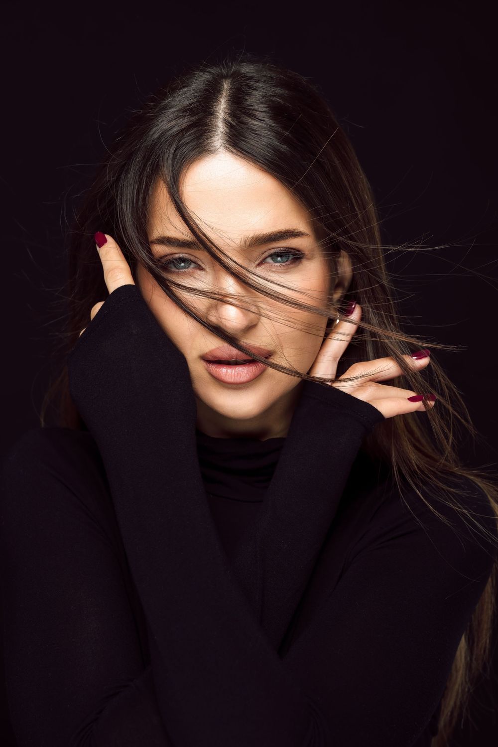Dramatic beauty portrait with windswept hair against dark background.