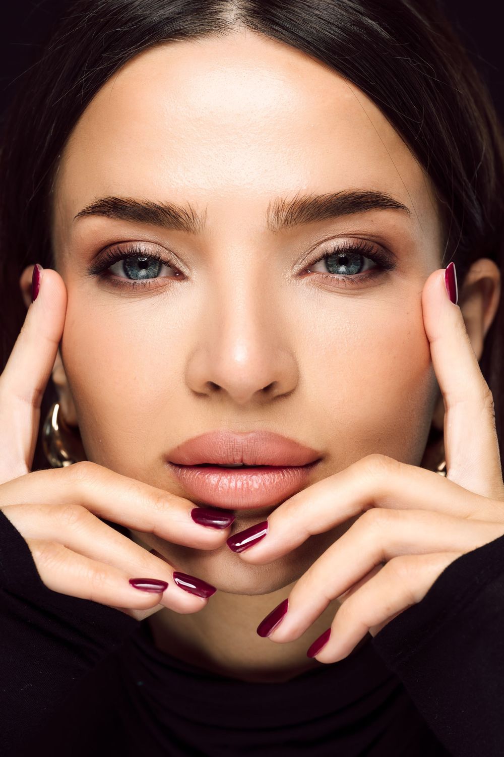 Close-up beauty shot showcasing manicured hands and natural makeup.