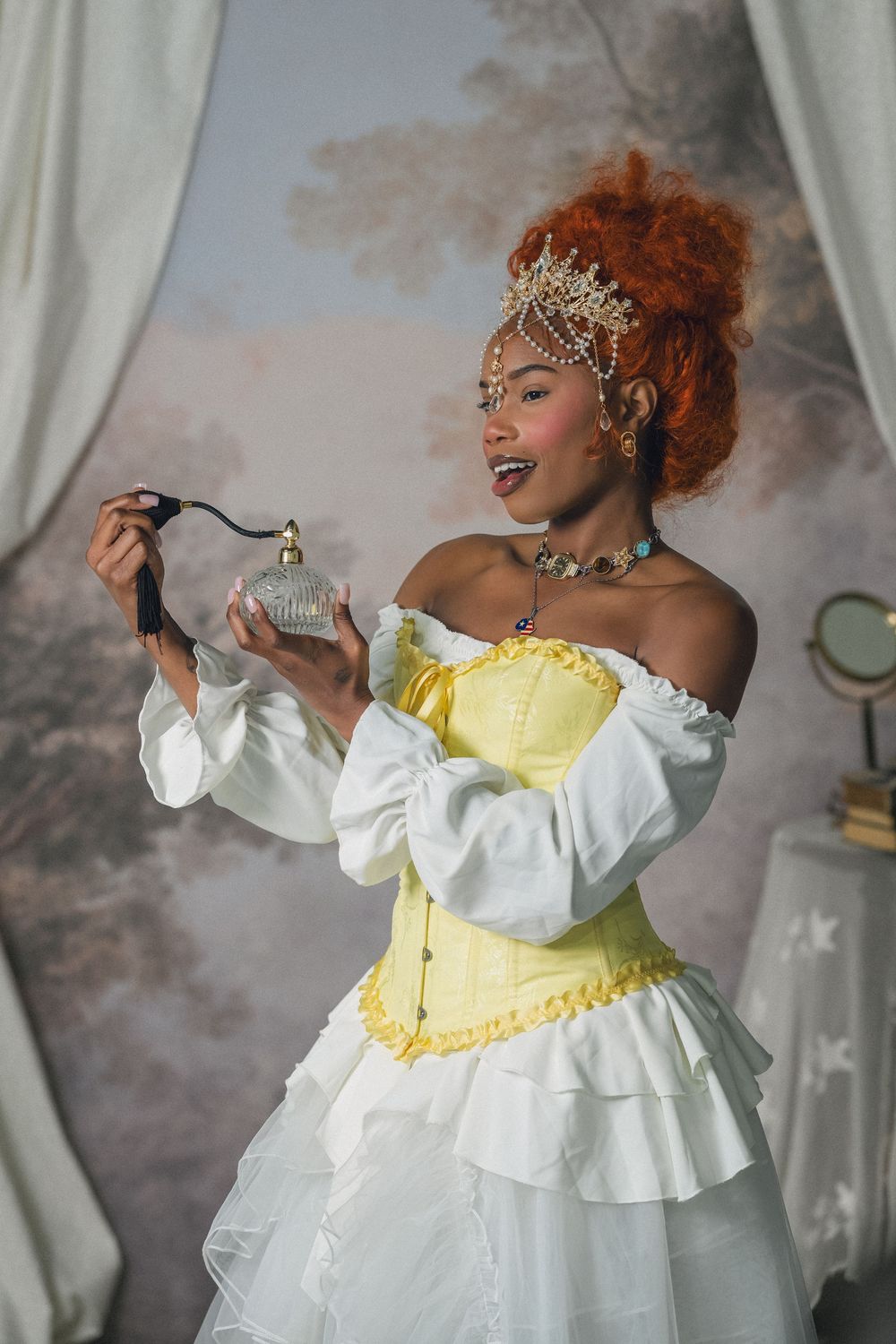Woman in yellow corset and white gown holding vintage perfume bottle with red curly hair and pearl crown.
