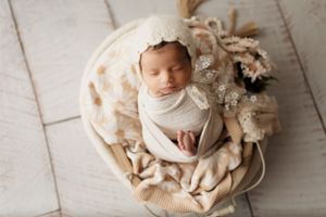Peaceful newborn sleeps on textured white blanket with floral decorations.