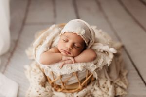 Newborn baby rests on cream colored textured blanket in artistic portrait setting.