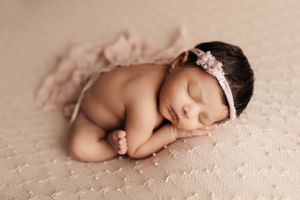 Sleeping newborn posed on soft pink textured backdrop in natural light.
