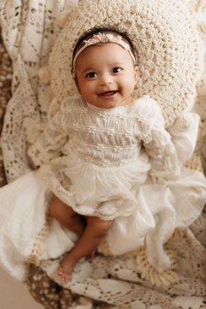 Baby in white lace dress smiles during professional portrait session.
