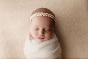 Sleeping newborn wrapped in soft fabric with delicate headband.