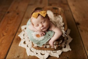 Newborn rests on vintage doily with mint and cream colored accessories.