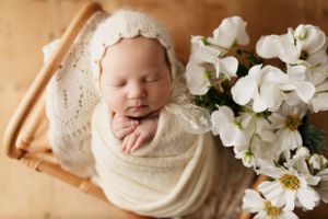 Sleeping newborn wrapped in cream fabric with white floral decorations.