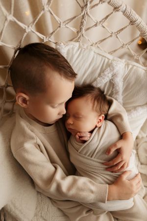 Two children in cream sweaters sharing a tender moment on white bedding.