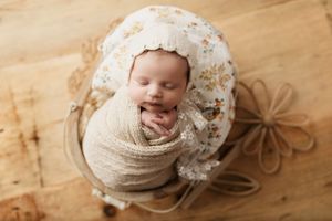 Newborn baby sleeping peacefully on wooden floor with delicate floral accents.