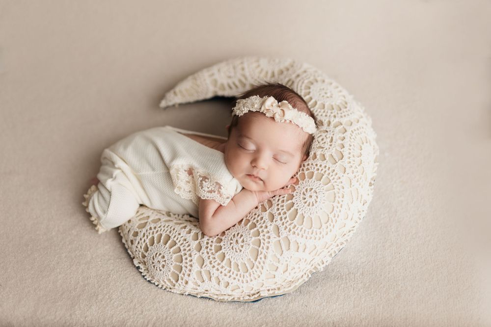 Sleeping newborn on cream textured blanket with lace details.