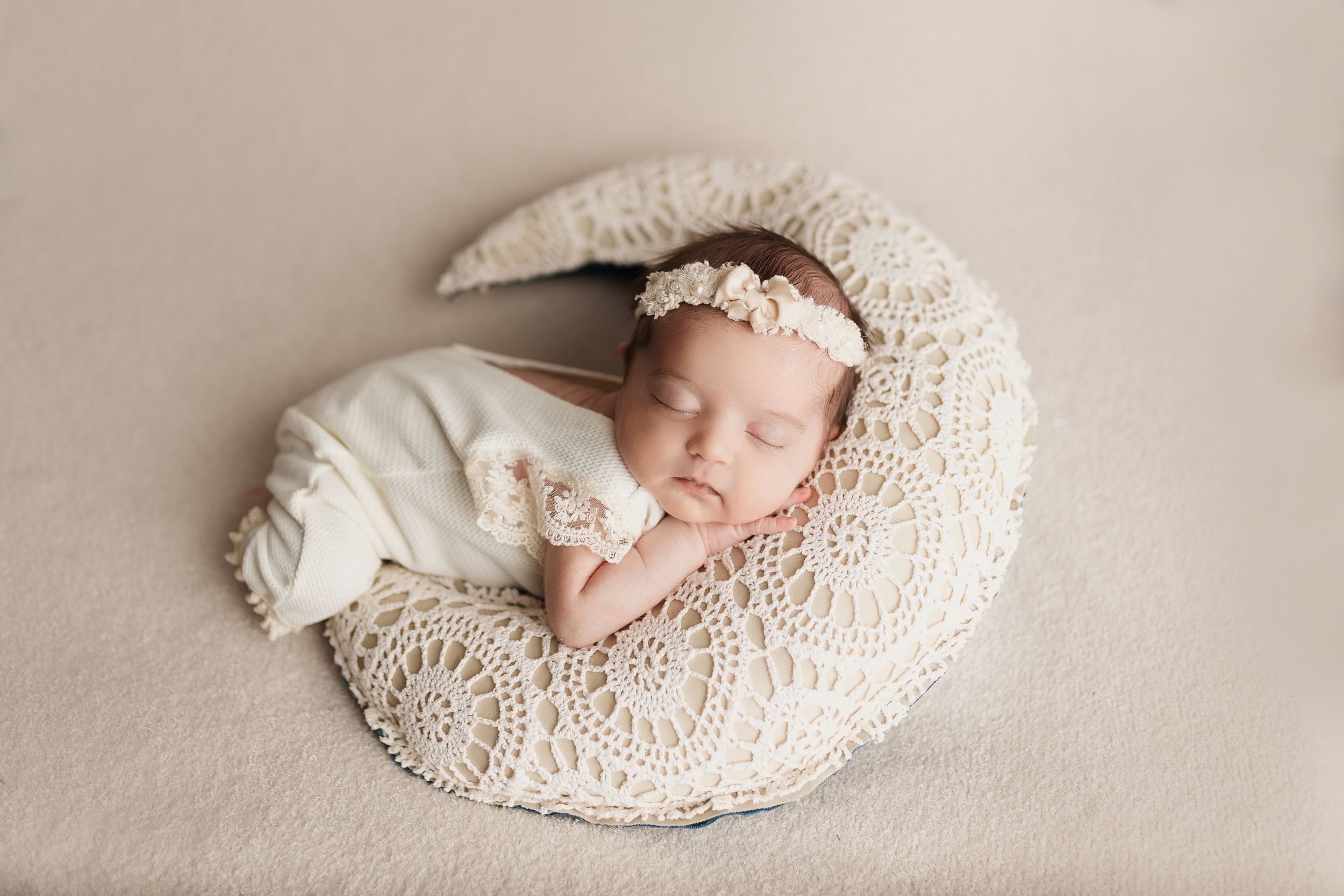 Sleeping newborn on cream textured blanket with lace details.