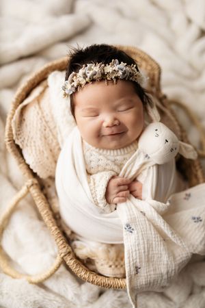 Newborn baby peacefully sleeping in cozy white blankets with small stuffed animal toy.