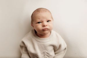 Baby in cream sweater against white background showing various expressions.
