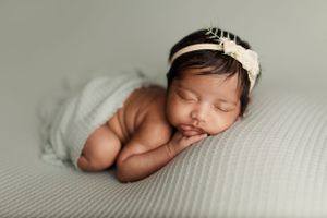 Newborn baby sleeping peacefully on soft white textured blanket in natural light.