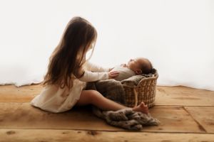 Baby in soft pink outfit resting on wooden floor during professional photoshoot.