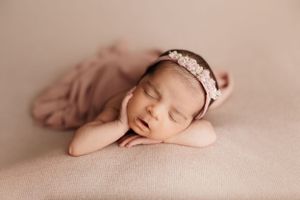Artistic newborn photography with baby in soft pink tones and lace accessories.