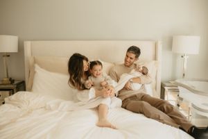 Family cuddles together on white bed during lifestyle photoshoot.