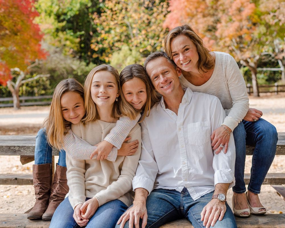 Happy family of five posing on a bench surrounded by colorful autumn foliage in a park.