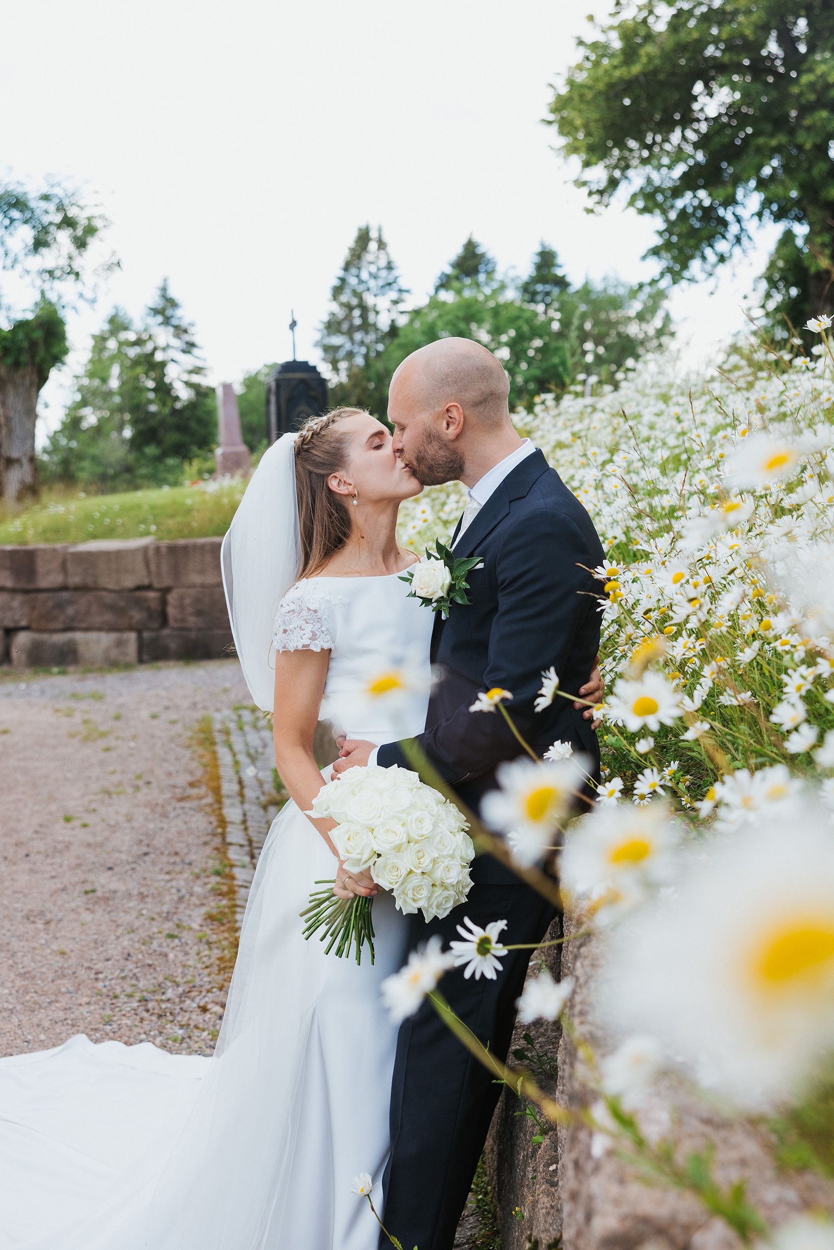 Halvfigursbilde av brudepar som kysser blant prestekrager