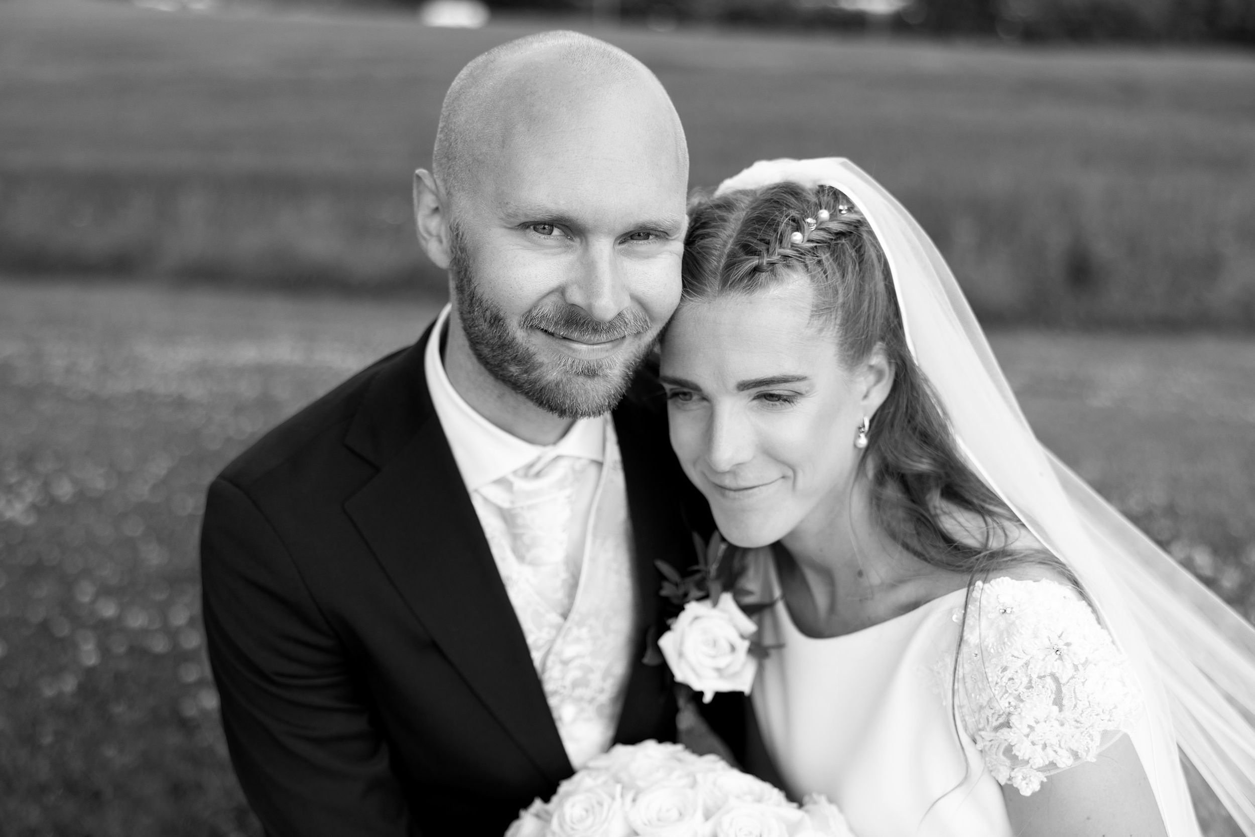 Sort-hvitt bilde av brudgom som ser i kamera. Bruden lener seg på brudgommens skulder.
