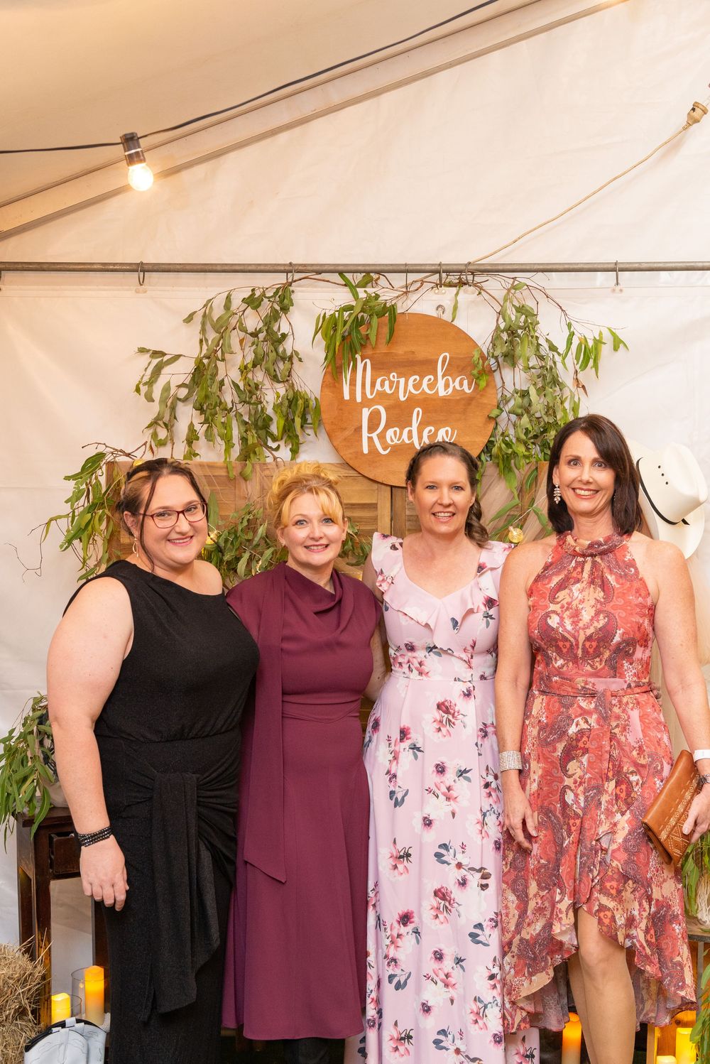 Four friends posing together at a social gathering with greenery and decor in the background.