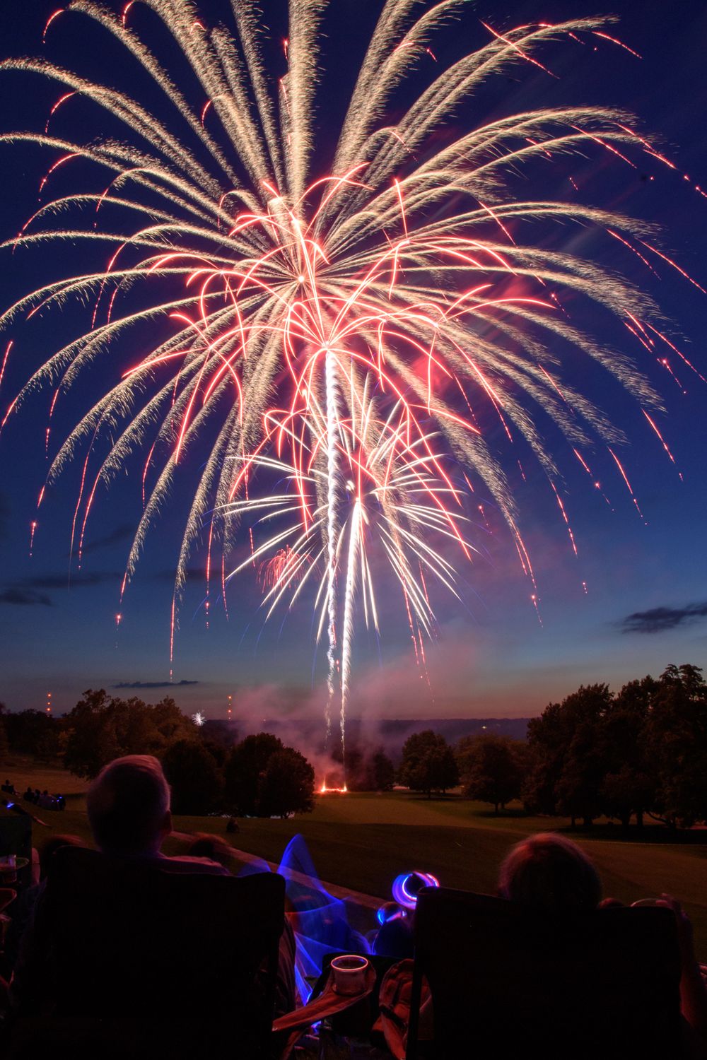 Red and white fireworks burst across a dark night sky during a celebration.