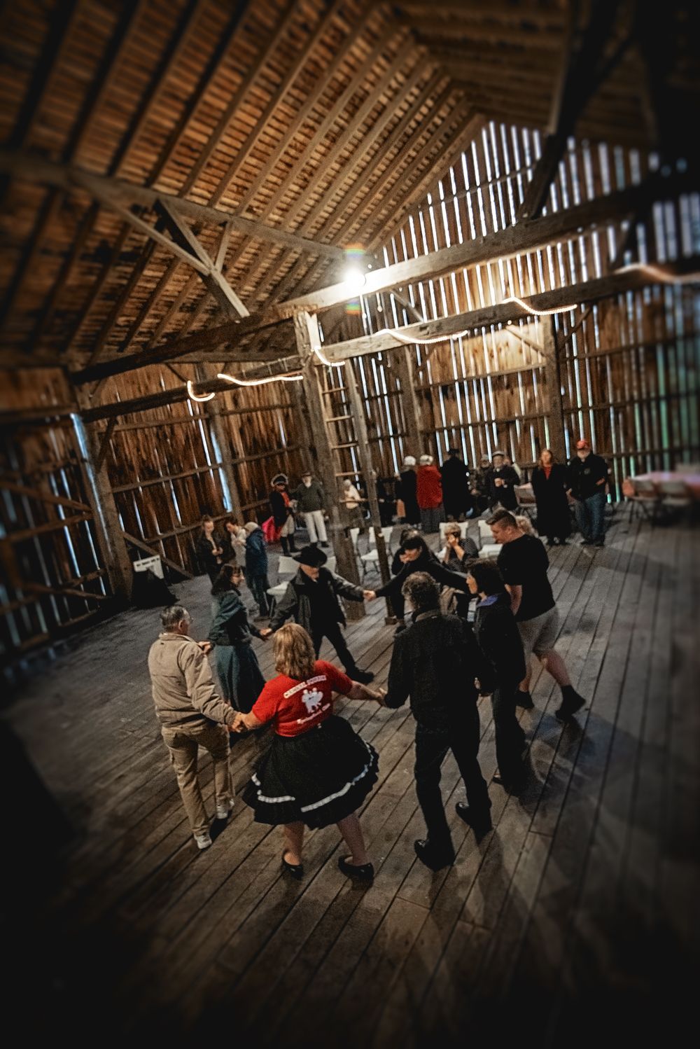 People gathered in a rustic wooden barn with sunlight streaming through the rafters during an event.