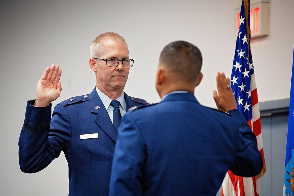 Military service members taking oath during official ceremony with American flag in background.