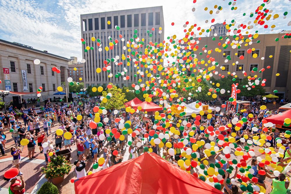 Massive balloon release with thousands of colorful balloons floating up against modern city buildings.