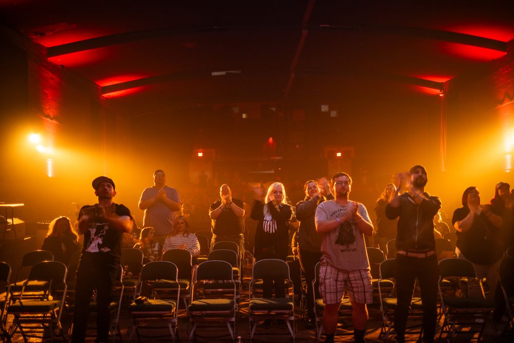 Performers standing in silhouette on stage with dramatic red and orange lighting creating a moody concert atmosphere.