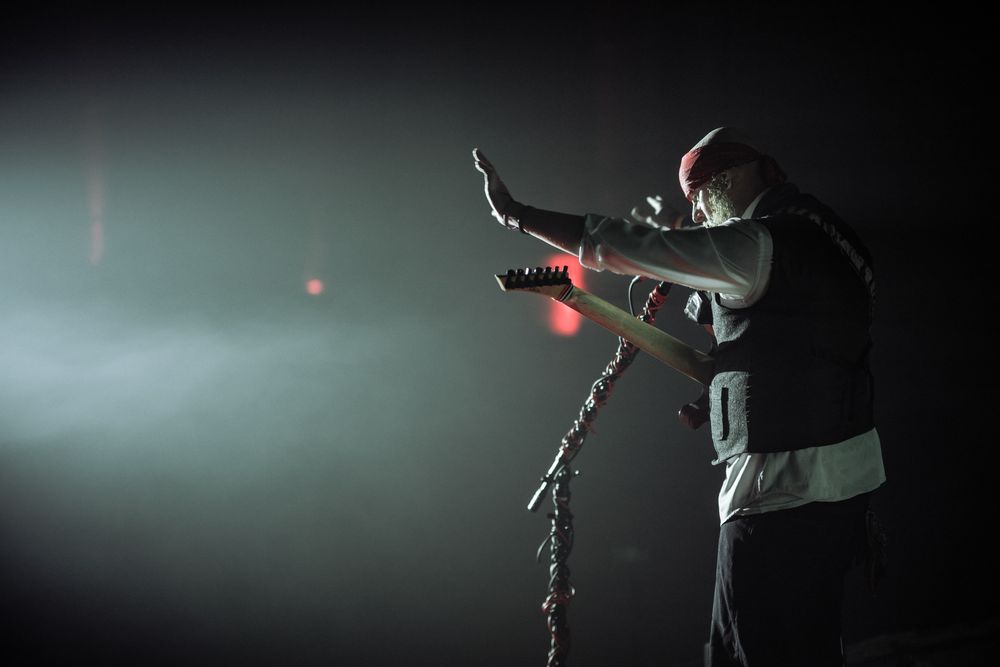 Silhouetted performer in black dances expressively on stage backlit by dramatic spotlights and atmospheric fog.
