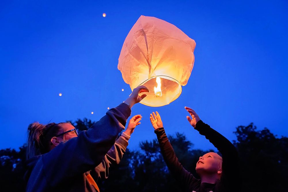 Paper lanterns being released into a dark blue sky at dusk.