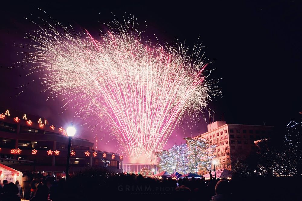Spectacular pink fireworks display lighting up the night sky over a dark horizon.