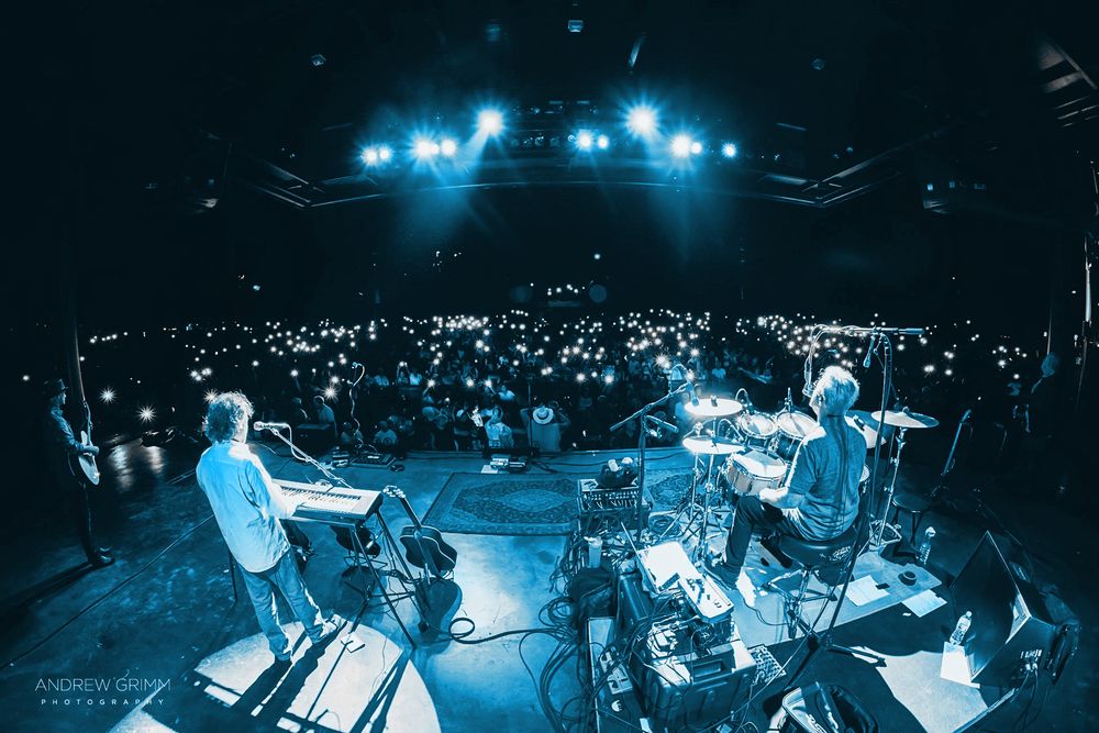 Concert venue with blue stage lighting and audience silhouettes visible.
