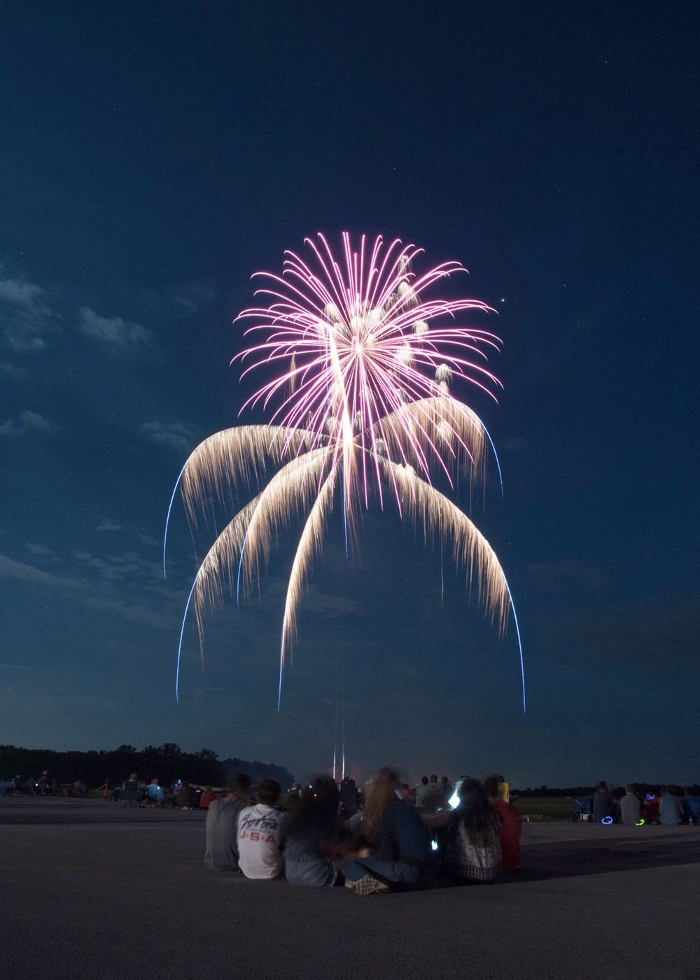 Pink and white fireworks bursting over a rural landscape at night.