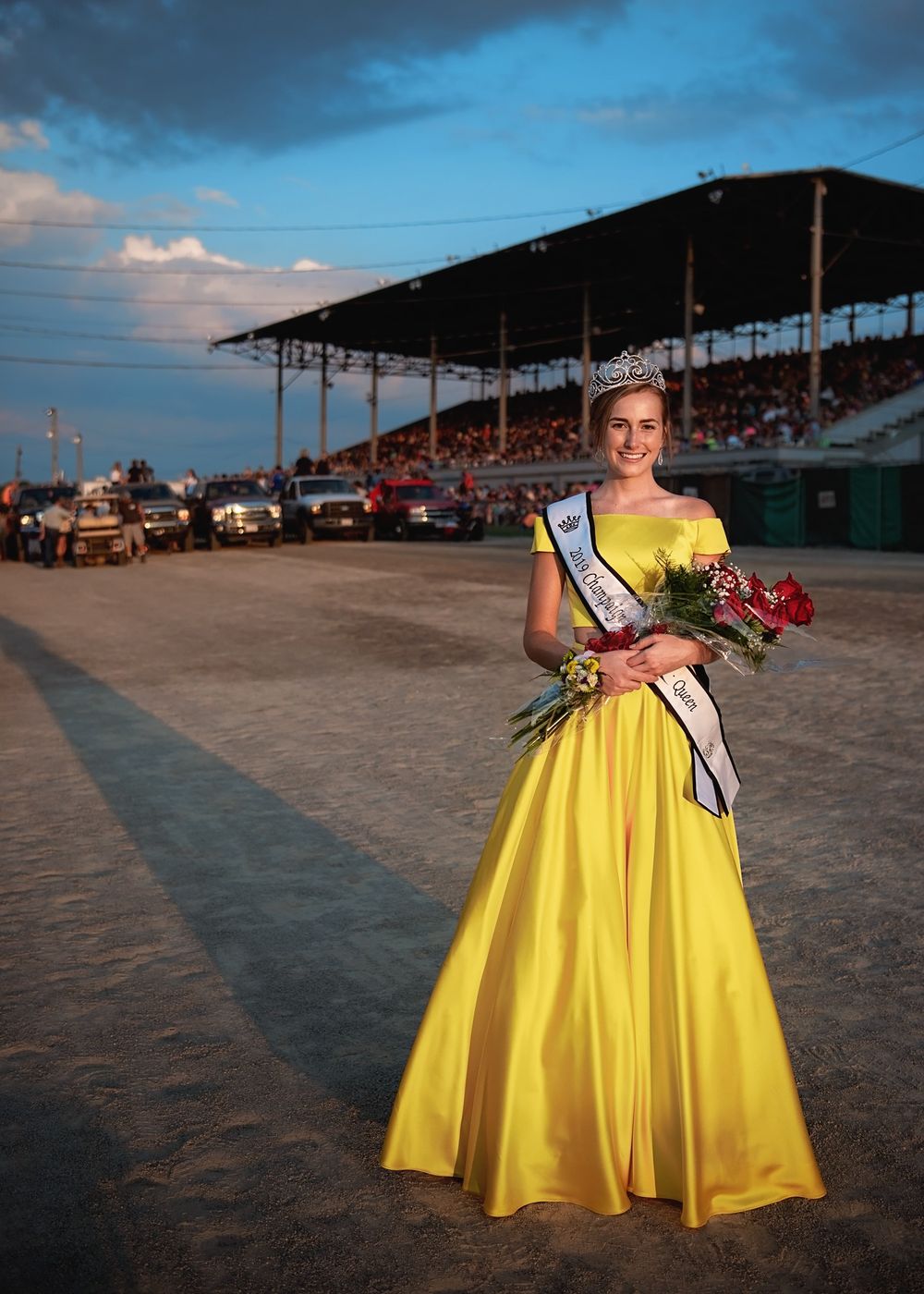 Person in yellow gown posing on dirt track at outdoor venue.