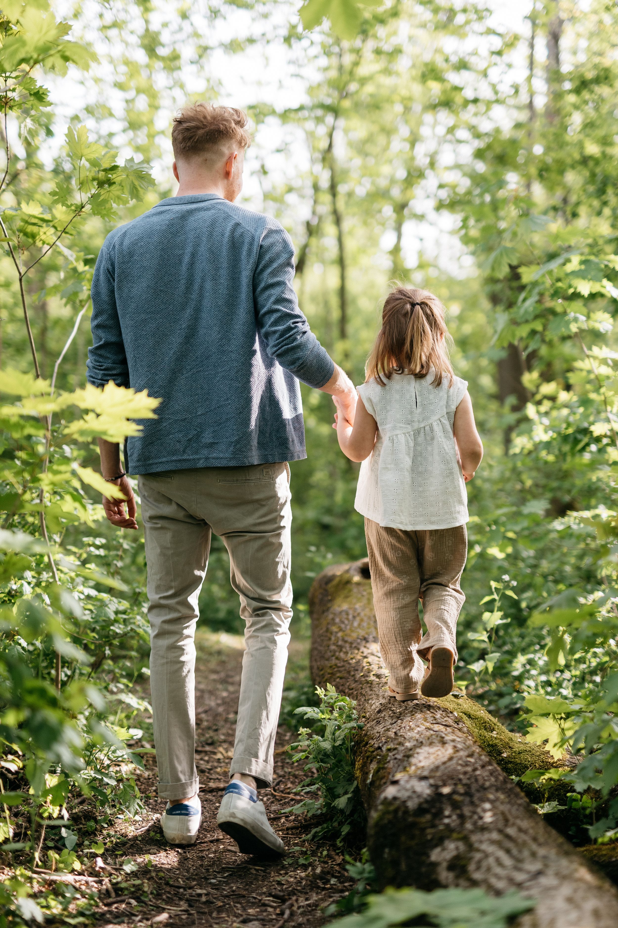 Natürliches ungestelltes Familienfoto draußen im Park. Papa und Tochter balancieren auf Baumstamm.