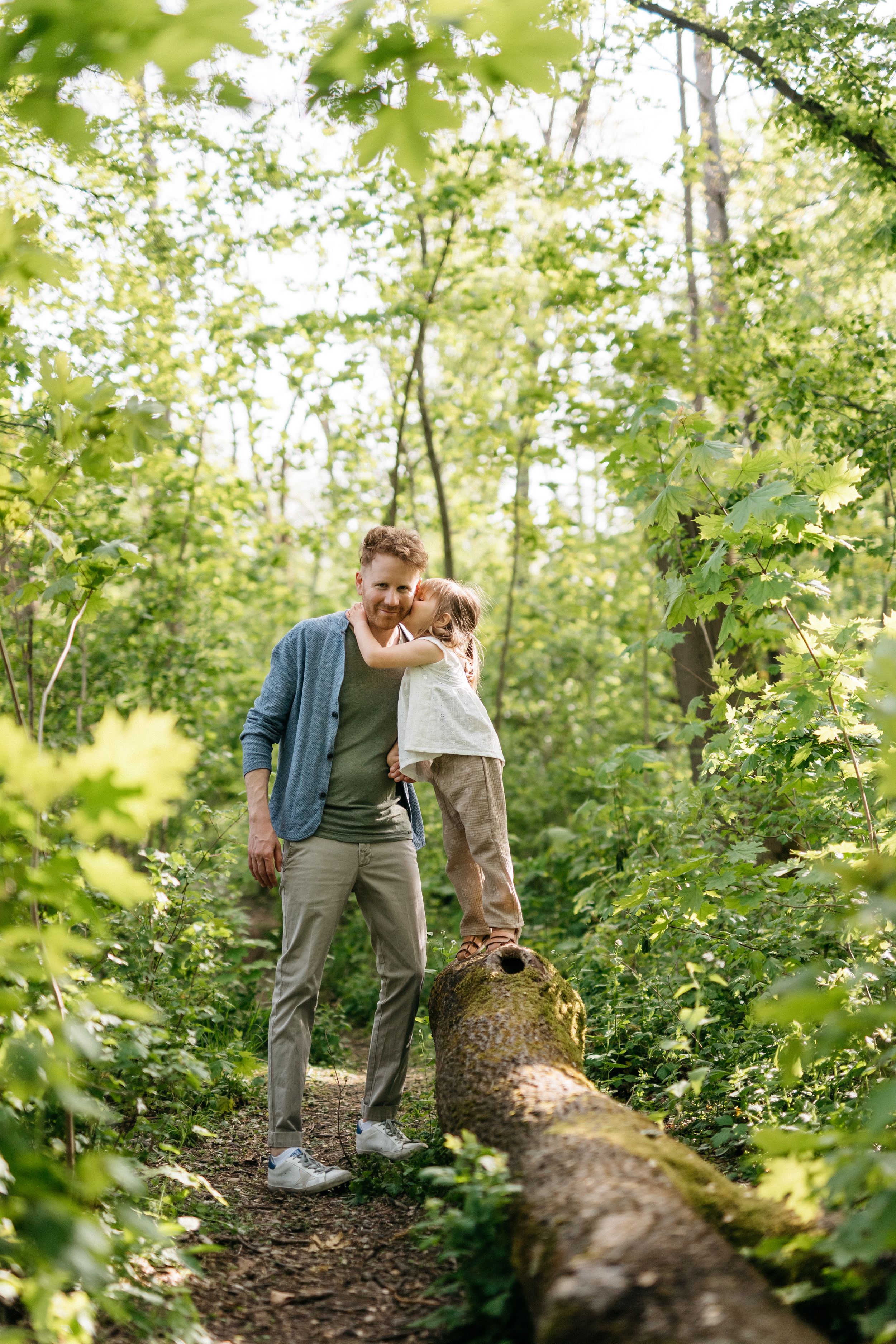 Natürliches ungestelltes Familienfoto draußen im Park. Tochter gibt Papa ein Bussi.