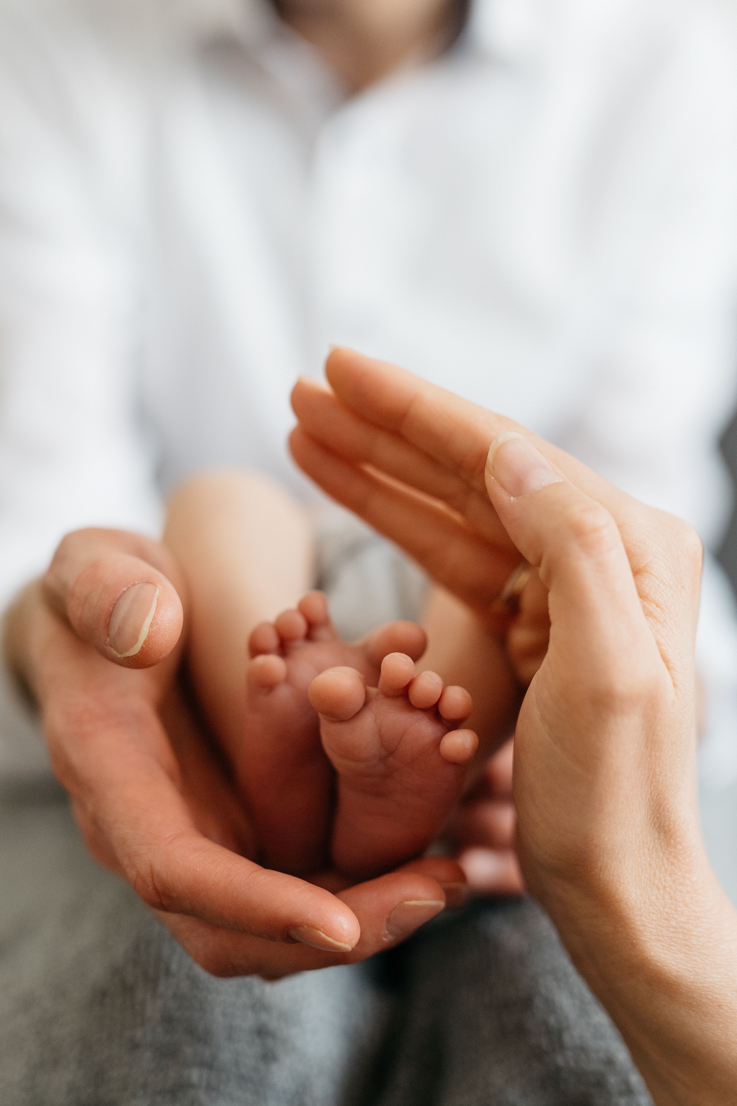 Süße Babyfüsse, die von Mamas und Papas Hand eingerahmt werden